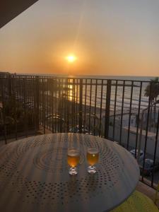 a table with two wine glasses on a balcony with the sunset at Beautiful Apartment on The First Line of The Sea in Haifa