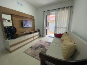 a living room with a couch and a tv at Apto na praia de Palmas, climatizado, com piscina, próximo ao mar e com jardim privativo in Governador Celso Ramos