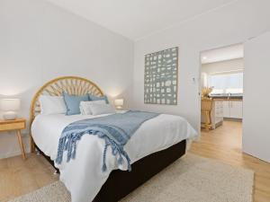 a white bedroom with a large bed with blue pillows at Husky Beach House by Experience Jervis Bay in Huskisson