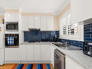 une cuisine avec des placards blancs et du carrelage bleu dans l'établissement Jacaranda Cottage 5A Nelson Street, à Nelson Bay 4 autres photos