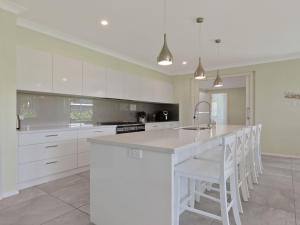 a kitchen with white cabinets and a kitchen island with white chairs at Pollys in Callala Bay