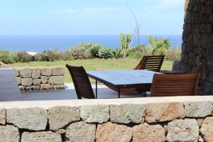 una mesa y sillas en un patio con una pared de piedra en IL VIGNETO en Pantelleria
