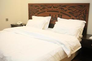 un grande letto con lenzuola bianche e testiera in legno di Al Khuzama Resort a Taif