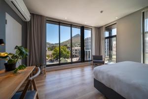 a bedroom with a bed and a desk and large windows at Kloof Street Hotel - Lion Roars Hotels & Lodges in Cape Town