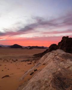 a rock in the desert with a sunset in the background at Wadi Rum Quiet Village Camp in Wadi Rum