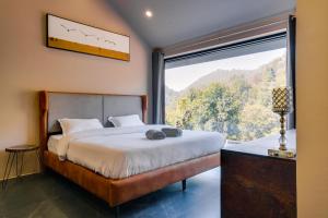 a bedroom with a bed and a large window at SaffronStays Elysian, Dehradun - best mountain views from this party - All clear roads in Dehradun