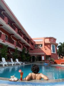 Un homme se posant dans une piscine à côté d'un bâtiment dans l'établissement Jasminn Hotel - AM Hotel Kollection, à Betalbatim