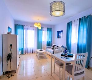 ein Wohnzimmer mit einem Tisch und ein Wohnzimmer mit blauen Vorhängen in der Unterkunft La Graciosa Mykonos Beach, Junior Suite in Caleta de Sebo