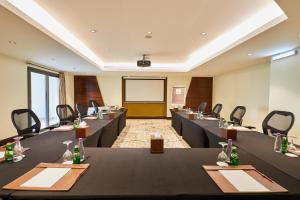 une salle de conférence avec des tables et des chaises noires et un écran dans l'établissement Crowne Plaza Riyadh Al Waha, an IHG Hotel, à Riyad