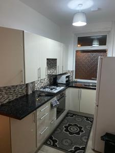 cocina con armarios blancos y encimera negra en Lovely 2 Bedroom Apartment with free parking en Mánchester