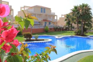 a swimming pool in front of a house with flowers at 2 bedroom Duplex Apartment Playa Flamenca in Orihuela Costa +3 photos