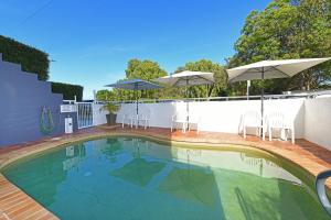 a swimming pool with chairs and umbrellas on a patio at Belvedere Apartments in Caloundra
