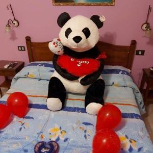 a stuffed panda bear sitting on a bed with balloons at Hotel Caribe in Casalnuovo di Napoli
