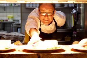 a man in a kitchen preparing plates on a table at Hotel Greetsiel in Greetsiel