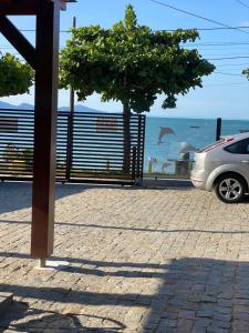 a car parked next to the ocean with a fence at Apartamento Frente Mar na Baía de Porto Belo in Porto Belo