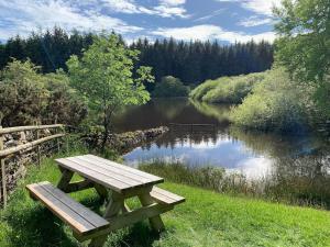 a wooden picnic table sitting next to a lake at The Stables at Pentregaer Ucha, tennis court & lake in Oswestry