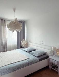 a white bedroom with a bed and a chandelier at Bel Appartement near Bâle Mulhouse Airport in Saint-Louis
