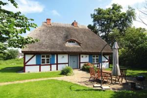 a house with a thatched roof with chairs and an umbrella at Ferienwohnung Dycke Haus, Zudar in Zudar