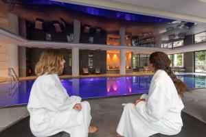 two women in white robes sitting next to a swimming pool at Rivage Hôtel & Spa Annecy in Annecy