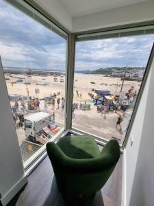 a green chair sitting in front of a window with a beach at Chy Mor Apartment 1 in St Ives