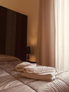 1 cama con toallas blancas y ventana en Motta Palace Apartments & Rooms, en Motta SantʼAnastasia