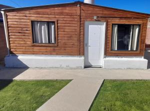 a wooden cabin with a door and a grass yard at M&M l in Comodoro Rivadavia