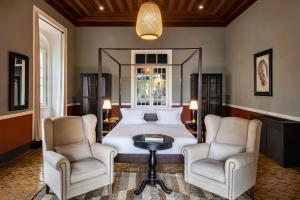 a bedroom with a large bed with two chairs and a table at Hotel Roça Sundy in Santo António