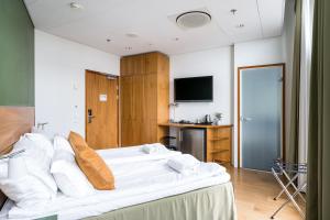 um quarto com uma cama com lençóis brancos e uma televisão em Hiisi Hotel Helsinki Jätkäsaari em Helsínquia