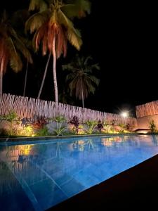 a swimming pool at night with a fence and palm trees at PATACHO VILLE - Rota Ecológica dos MILAGRES in Pôrto de Pedras