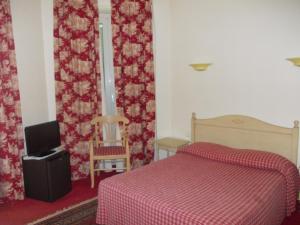a bedroom with a bed and a tv and curtains at Hotel Marcellin in Beaulieu-sur-Mer