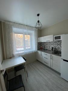ケメロヴォにあるАпартаменты Тухачевского 2の白いキャビネットとテーブル、窓付きのキッチン