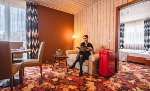 eine Frau auf einer Couch in einem Hotelzimmer mit Koffer in der Unterkunft Hotel Lajta Park in Mosonmagyaróvár