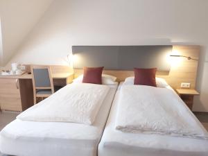 a bedroom with two beds with white sheets and red pillows at Pension Heuer in Brietlingen