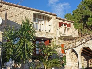 a stone house with a balcony and a palm tree at Apartments Račić in Bol