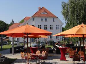 eine Gruppe von Tischen und Stühlen mit orangefarbenen Sonnenschirmen in der Unterkunft Hotel und Restaurant Am Peenetal in Liepen