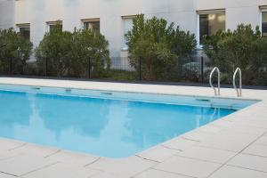 - une piscine d'eau bleue en face d'un bâtiment dans l'établissement Aparthotel Adagio Access Bordeaux Rodesse, à Bordeaux