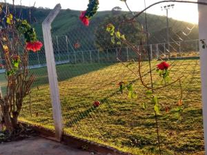 a fence with red flowers on it next to a field at Pousada Recanto Dos Tucanos in Capitólio
