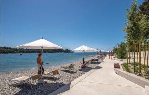 a beach with chairs and umbrellas and people on the beach at Amazing Home In Rovinj With 2 Bedrooms And Outdoor Swimming Pool in Spanidiga