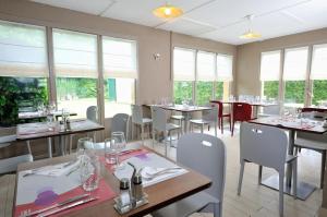 una sala da pranzo con tavoli, sedie e finestre di Kyriad Direct Soissons a Soissons