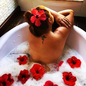 a woman laying in a bath tub with red flowers in it at Prana Guest House in Praia do Rosa