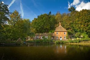 a large brick house next to a river with trees at Leeds Castle Holiday Cottages in Maidstone