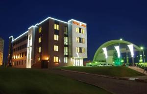 a hotel at night with a building in the foreground at Hotel Krokus in Naberezhnyye Chelny