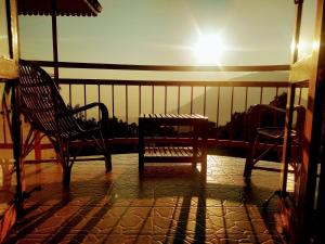 Un balcón con 2 sillas, una mesa y el sol en Deshadan Mountain Resort -The highest resort in Munnar, en Munnar