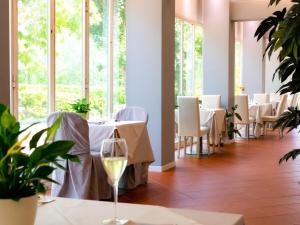 restauracja z białymi stołami, krzesłami i oknami w obiekcie Hotel Castello Artemide Congressi w mieście Castel San Pietro Terme