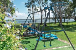einen Spielplatz mit drei Schaukeln in einem Park in der Unterkunft Getaway Lakefront Environmental House on Lake Macquarie with Water View in Lake Munmorah