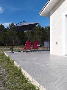 two red chairs and an umbrella on a patio at Villa en bordure de forêt . in Onesse-et-Laharie