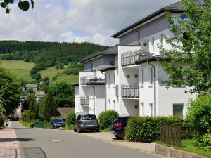een wit gebouw met auto's ervoor geparkeerd bij Geräumiges Apartment mit Balkon in Willingen in Willingen