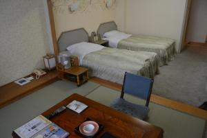 a room with two beds and a table and a chair at Hotel Akankoso in Akankohan