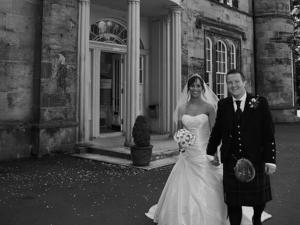 uma noiva e um noivo a sair de um edifício em Kincaid House Hotel em Kirkintilloch