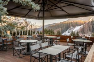 a dining area with tables, chairs and umbrellas at Faloria Mountain Spa Resort in Cortina dʼAmpezzo